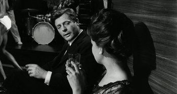 Movie still from “La Notte” (1961), directed by Michelangelo Antonioni – A man and a woman sitting at a table with a glass of wine; Medium shot, Over the shoulder angle