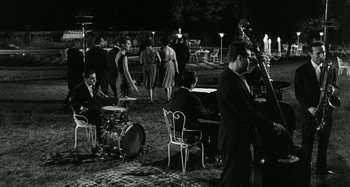 Movie still from “La Notte” (1961), directed by Michelangelo Antonioni – A black and white photo of a group of people playing music; Wide shot, High angle