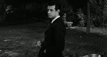 Movie still from “La Notte” (1961), directed by Michelangelo Antonioni – A black and white photo of a man smoking a cigarette; Medium shot, Low angle