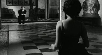 Movie still from “La Notte” (1961), directed by Michelangelo Antonioni – A woman standing in front of another woman in front of a building; Wide shot, Over the shoulder angle