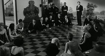 Movie still from “La Notte” (1961), directed by Michelangelo Antonioni – Black and white photograph of people sitting in a circle; Wide shot, High angle