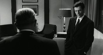 Movie still from “La Notte” (1961), directed by Michelangelo Antonioni – A man in a suit and tie standing next to another man in a suit and tie; Medium shot, Over the shoulder angle