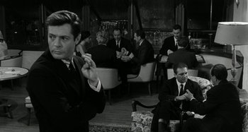 Movie still from “La Notte” (1961), directed by Michelangelo Antonioni – A group of men in suits and ties sitting in a room; Medium shot, Over the shoulder angle