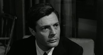 Movie still from “La Notte” (1961), directed by Michelangelo Antonioni – Black and white photograph of a man wearing a suit; Close Up shot, Over the shoulder angle