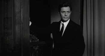 Movie still from “La Notte” (1961), directed by Michelangelo Antonioni – A black and white photo of a man wearing a suit and tie; Close Up shot, Over the shoulder angle