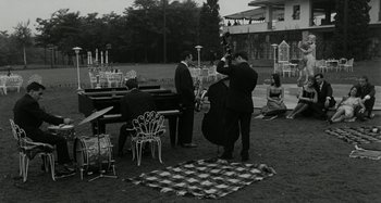 Movie still from “La Notte” (1961), directed by Michelangelo Antonioni – A black and white photo of a band playing in a park; Extreme Wide shot, High angle