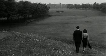 Movie still from “La Notte” (1961), directed by Michelangelo Antonioni – A black and white photo of a man in a suit walking on a field; Extreme Wide shot, High angle