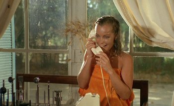Movie still from “The Swimming Pool” (1969), directed by Jacques Deray – A woman in an orange towel is holding a phone; Medium shot, High angle