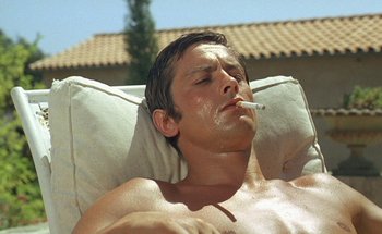 Movie still from “The Swimming Pool” (1969), directed by Jacques Deray – A man laying down with a cigarette in his mouth; Close Up shot, Low angle