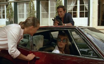 Movie still from “The Swimming Pool” (1969), directed by Jacques Deray – A man and a woman in a red car with another man in a red car; Medium shot, Over the shoulder angle