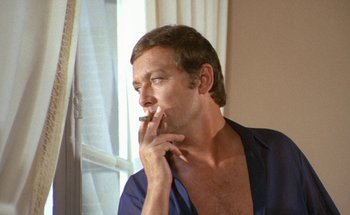 Movie still from “The Swimming Pool” (1969), directed by Jacques Deray – A man smoking a cigarette in front of a window; Close Up shot, Low angle