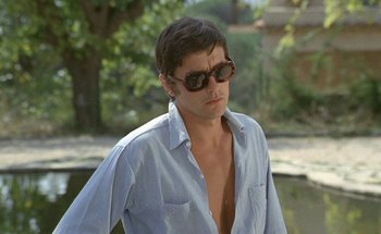 Movie still from “The Swimming Pool” (1969), directed by Jacques Deray – A man wearing sunglasses and a blue shirt; Close Up shot, Low angle