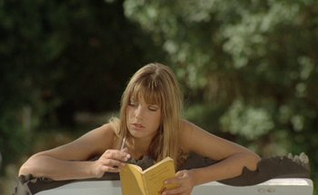 Movie still from “The Swimming Pool” (1969), directed by Jacques Deray – A woman reading a book while sitting on a bench; Medium shot, High angle