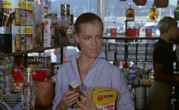 Movie still from “The Swimming Pool” (1969), directed by Jacques Deray – A woman in a store looking at a box of food; Medium shot, Low angle