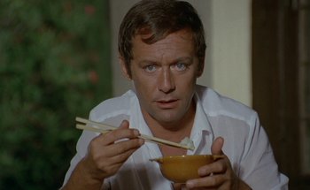 Movie still from “The Swimming Pool” (1969), directed by Jacques Deray – A man holding chopsticks while holding a bowl of food; Close Up shot, Low angle