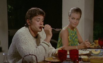 Movie still from “The Swimming Pool” (1969), directed by Jacques Deray – A man and a woman sitting at a dinner table; Medium shot, Low angle