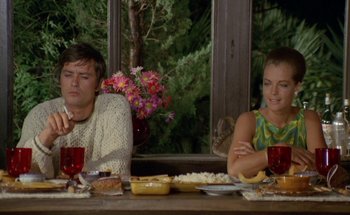 Movie still from “The Swimming Pool” (1969), directed by Jacques Deray – A man and a woman sitting at a dinner table; Medium shot, Over the shoulder angle