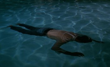 Movie still from “The Swimming Pool” (1969), directed by Jacques Deray – A man swimming in a pool at night; Wide shot, Overhead angle