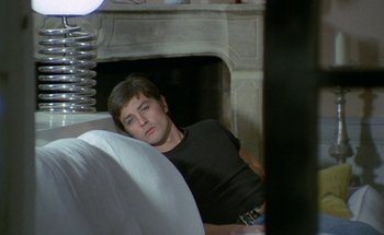 Movie still from “The Swimming Pool” (1969), directed by Jacques Deray – A man laying on the ground in front of a fireplace; Medium shot, High angle
