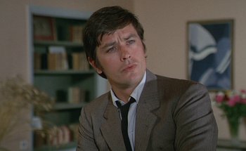 Movie still from “The Swimming Pool” (1969), directed by Jacques Deray – A man wearing a suit and tie sitting in front of a book shelf; Close Up shot, Low angle
