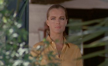 Movie still from “The Swimming Pool” (1969), directed by Jacques Deray – A woman wearing a yellow shirt standing next to a bush; Close Up shot, Low angle