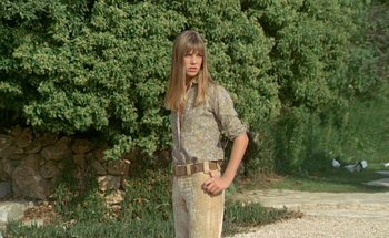 Movie still from “The Swimming Pool” (1969), directed by Jacques Deray – A man with long blond hair standing in front of a tree; Medium shot, Low angle
