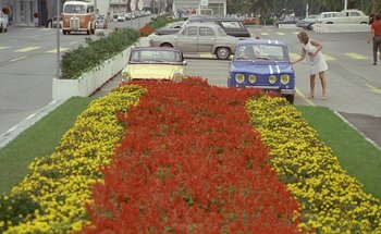 Movie still from “The Swimming Pool” (1969), directed by Jacques Deray – Cars parked on the side of the road next to a flower bed; Wide shot, High angle