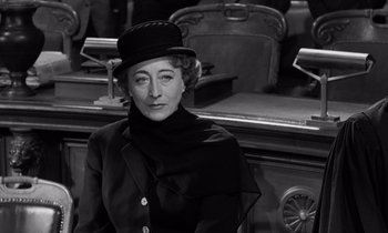 Movie still from “The Truth” (1960), directed by Henri-Georges Clouzot – An older woman wearing a black hat and a black coat; Close Up shot, Over the shoulder angle