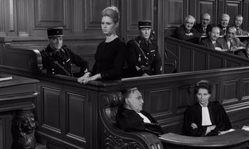 Movie still from “The Truth” (1960), directed by Henri-Georges Clouzot – A woman sitting in a courtroom with a man sitting in a chair; Medium shot, Low angle