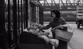 Movie still from “The Truth” (1960), directed by Henri-Georges Clouzot – A woman standing in front of a table filled with baskets; Medium shot, High angle