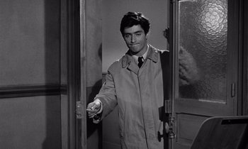 Movie still from “The Truth” (1960), directed by Henri-Georges Clouzot – A man in a trench coat is holding a remote control; Medium shot, Over the shoulder angle
