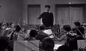 Movie still from “The Truth” (1960), directed by Henri-Georges Clouzot – A man standing in front of a group of people playing musical instruments; Medium shot, Low angle