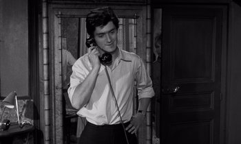 Movie still from “The Truth” (1960), directed by Henri-Georges Clouzot – A man talking on a phone while standing in front of a door; Medium shot, High angle