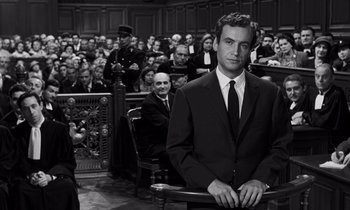 Movie still from “The Truth” (1960), directed by Henri-Georges Clouzot – A black and white photo of a man in a suit and tie in front of a group of people; Medium shot, High angle