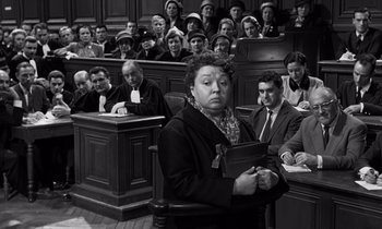 Movie still from “The Truth” (1960), directed by Henri-Georges Clouzot – An old photo of a woman in a court room holding a book; Medium shot, High angle