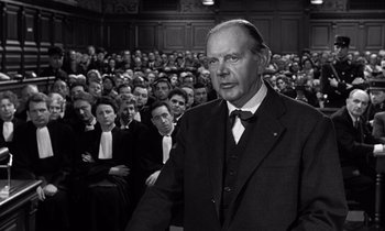 Movie still from “The Truth” (1960), directed by Henri-Georges Clouzot – An older man in a suit stands in front of a crowd; Medium shot, Over the shoulder angle