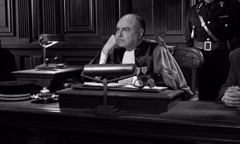 Movie still from “The Truth” (1960), directed by Henri-Georges Clouzot – A judge sitting at a table in a courtroom; Medium shot, High angle