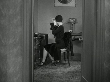 Movie still from “Ladies of Leisure” (1930), directed by Frank Capra – A woman sitting on a chair in front of a desk; Medium shot, High angle
