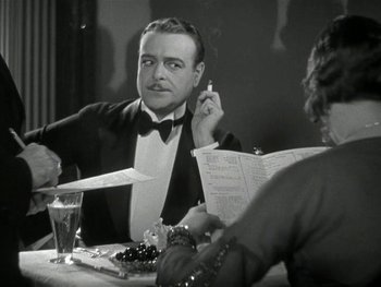 Movie still from “Ladies of Leisure” (1930), directed by Frank Capra – A black and white photo of a man smoking a cigarette at a dinner table; Close Up shot, Over the shoulder angle