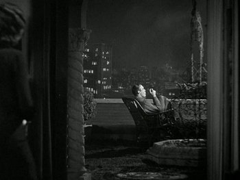 Movie still from “Ladies of Leisure” (1930), directed by Frank Capra – A man sitting in a chair on a porch at night; Wide shot, High angle