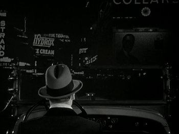 Movie still from “Ladies of Leisure” (1930), directed by Frank Capra – A man wearing a hat sitting in the driver's seat of a car; Medium shot, Over the shoulder angle