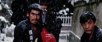Movie still from “Lady Snowblood” (1973), directed by Toshiya Fujita – A man in a black jacket is standing in the snow; Close Up shot, Low angle