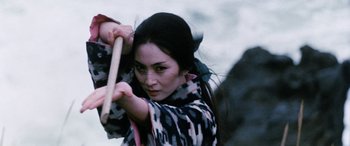 Movie still from “Lady Snowblood” (1973), directed by Toshiya Fujita – A woman holding a wooden stick in her hands; Close Up shot, Low angle