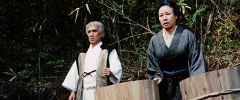Movie still from “Lady Snowblood” (1973), directed by Toshiya Fujita – A man and a woman standing next to each other in front of some trees; Medium shot, Low angle