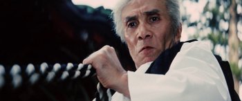 Movie still from “Lady Snowblood” (1973), directed by Toshiya Fujita – An older man holding a wooden stick in his hand; Close Up shot, Low angle