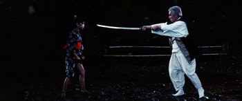 Movie still from “Lady Snowblood” (1973), directed by Toshiya Fujita – A man is holding a sword in front of a woman; Medium shot, Low angle