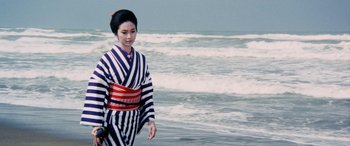 Movie still from “Lady Snowblood” (1973), directed by Toshiya Fujita – A geisha in a black and white striped outfit walking on the beach; Medium shot, Low angle