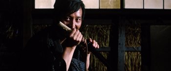 Movie still from “Lady Snowblood” (1973), directed by Toshiya Fujita – A man holding a knife and a banana in his mouth; Close Up shot, Low angle