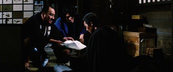 Movie still from “Lady Snowblood” (1973), directed by Toshiya Fujita – A group of people gathered around a man holding a box; Medium shot, High angle