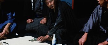Movie still from “Lady Snowblood” (1973), directed by Toshiya Fujita – A man sitting on the ground next to a table; Medium shot, High angle